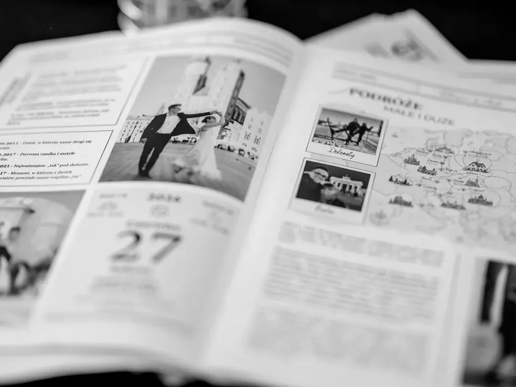 Rozłożona gazetka weselna na stole: zdjęcie pary tańczącej na krakowskim Rynku, ważne daty i mapa wspólnych podróży